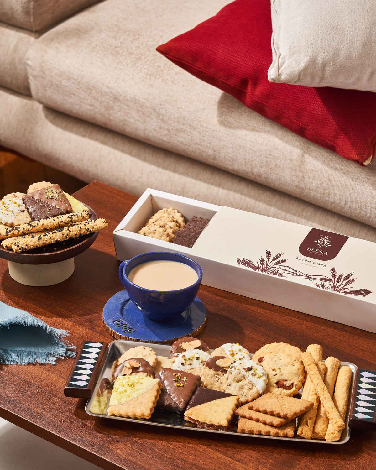 A tray of mixed biscuits and a Bléra box on a living-room table, beside a cup of tea
