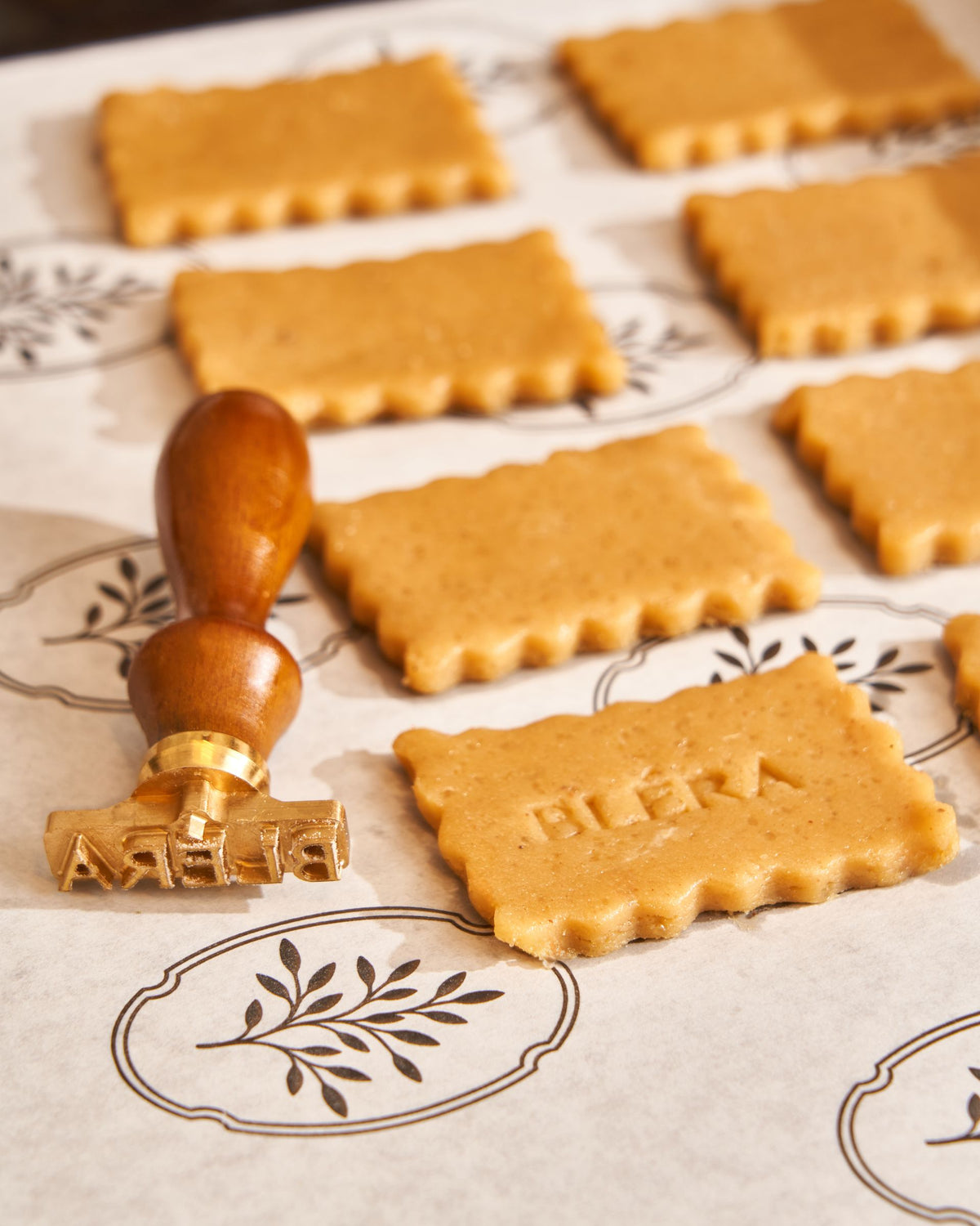 Rows of unbaked biscuits stamped with the Bléra name, the brass stamp resting beside them