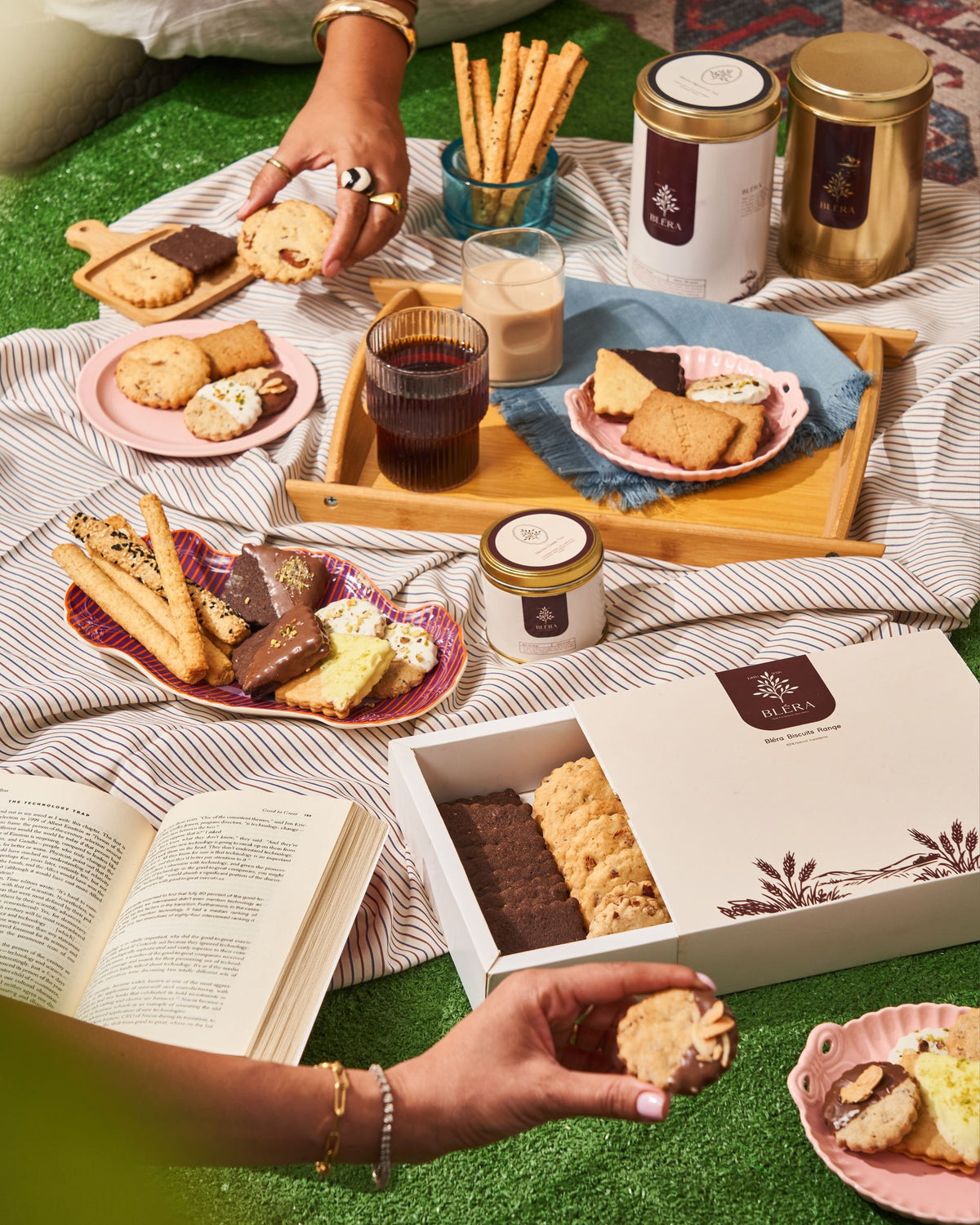 Golden tins, a jar of Signature sticks and plates of biscuits laid out on a picnic blanket