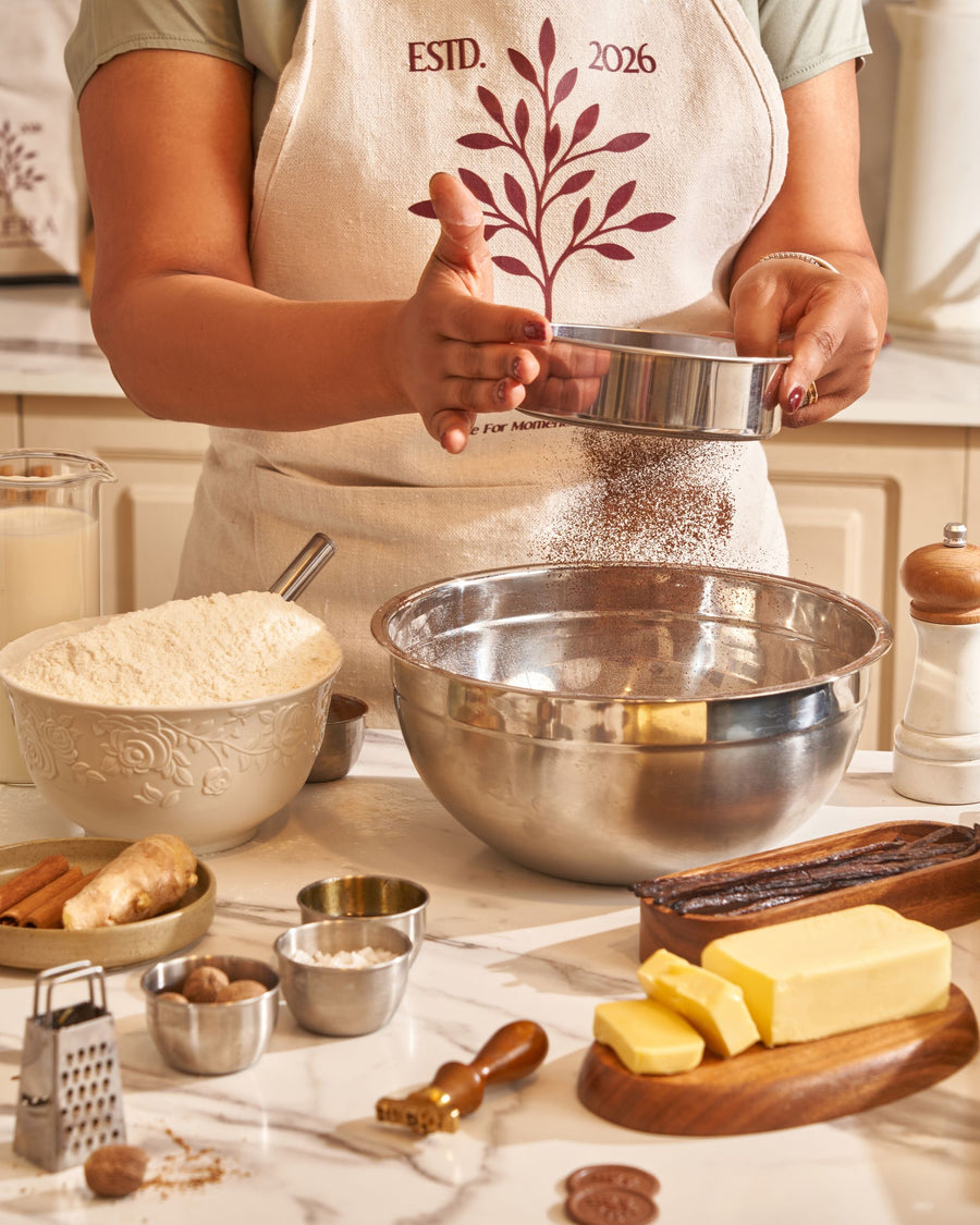 Flour sifted into a steel bowl by a baker in a Bléra apron